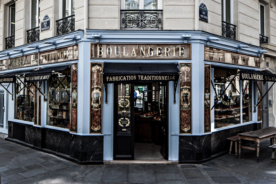 Historic corner storefront of Du Pain et des Idées bakery in Paris, with ornate 'Boulangerie' and 'Fabrication Traditionnelle' signage on painted glass panels and blue-trimmed woodwork.