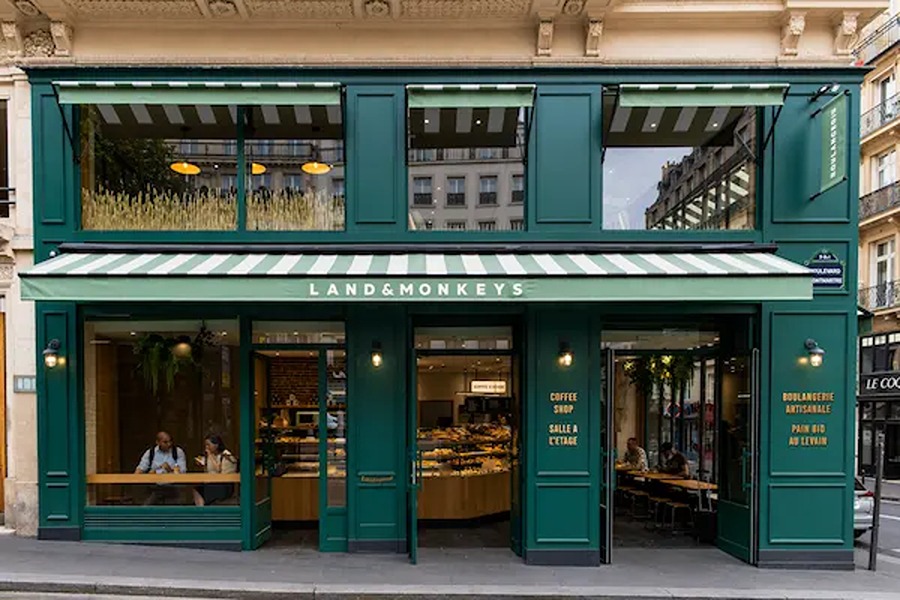 Green-façade storefront of Land & Monkeys bakery and coffee shop in Paris, with striped awnings, gold signage, and customers seated at window tables.
