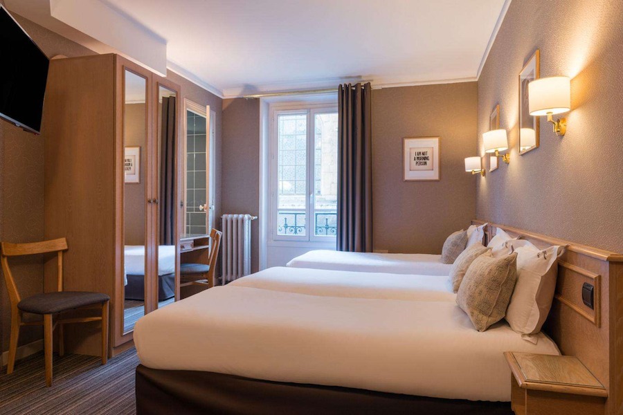 This is an image of a hotel bedroom with multiple beds and a muted colour palette.