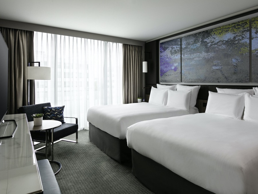 This is an image of a large hotel bedroom with two big double beds and big windows. It is minimalistic and modern in design.