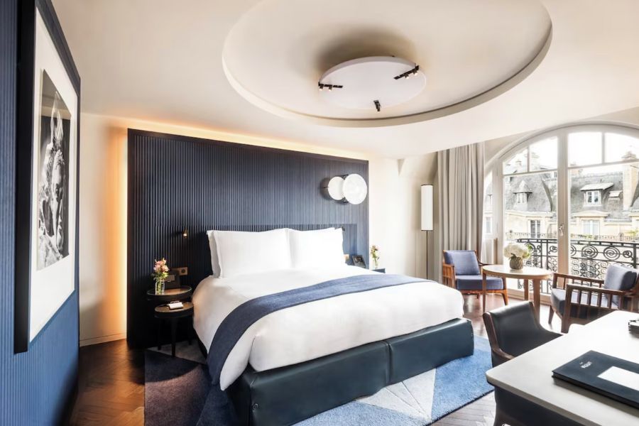 This is an image of a fancy hotel room in Paris. The window looks out on to other Parisian buildings and the accent colour for decor is navy.