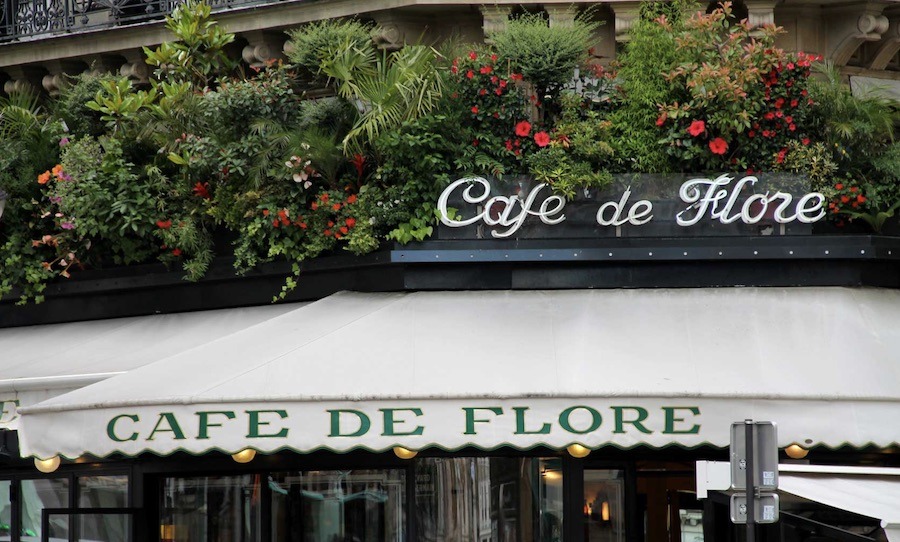 This is an image of the iconic exterior of Café de Flore with all the flowers around the sign.