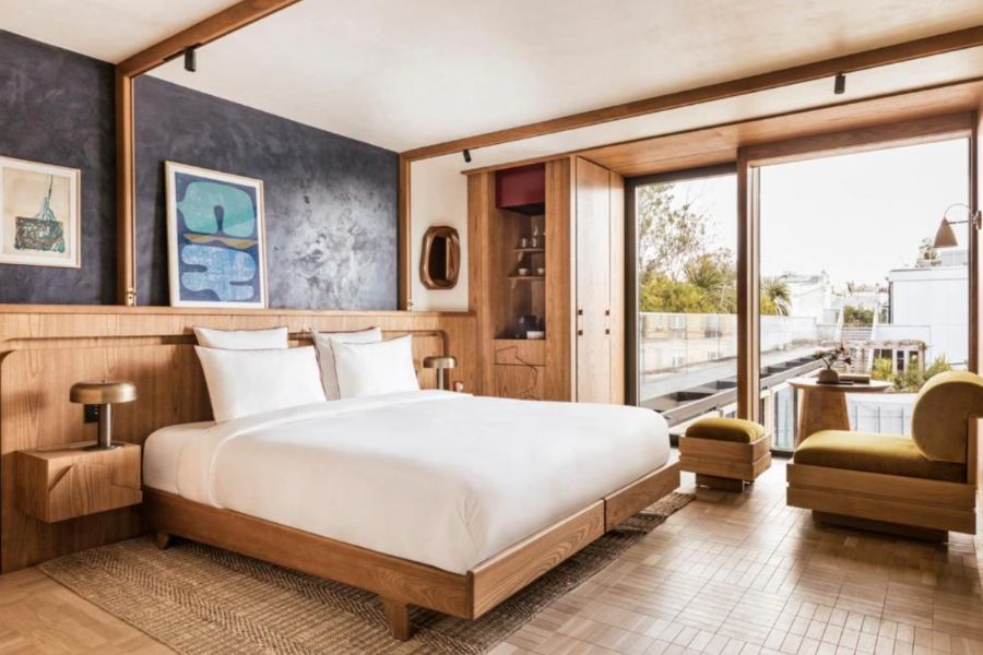 A hotel room in Paris with warm wood panelling, a slate blue feature wall, original artwork and sliding glass doors opening onto a terrace