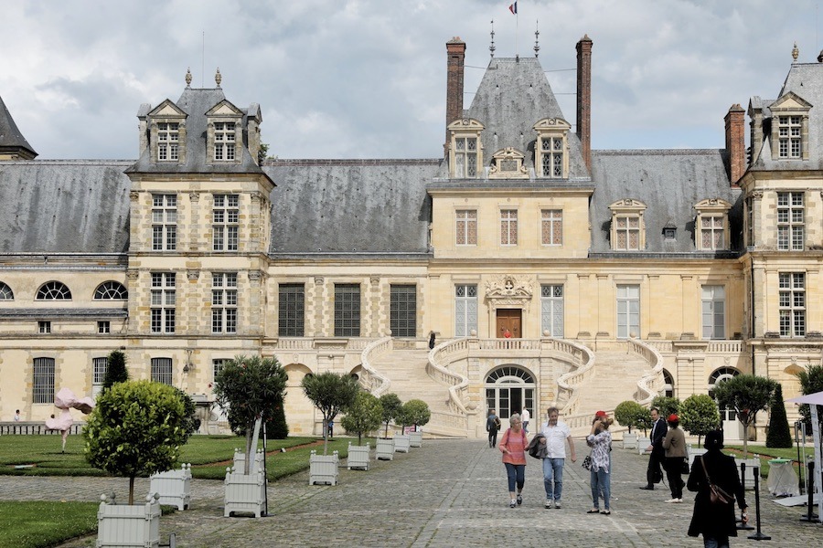 This is an image of the Chateau of Fontainebleau with people walking down in front of it to take pictures.