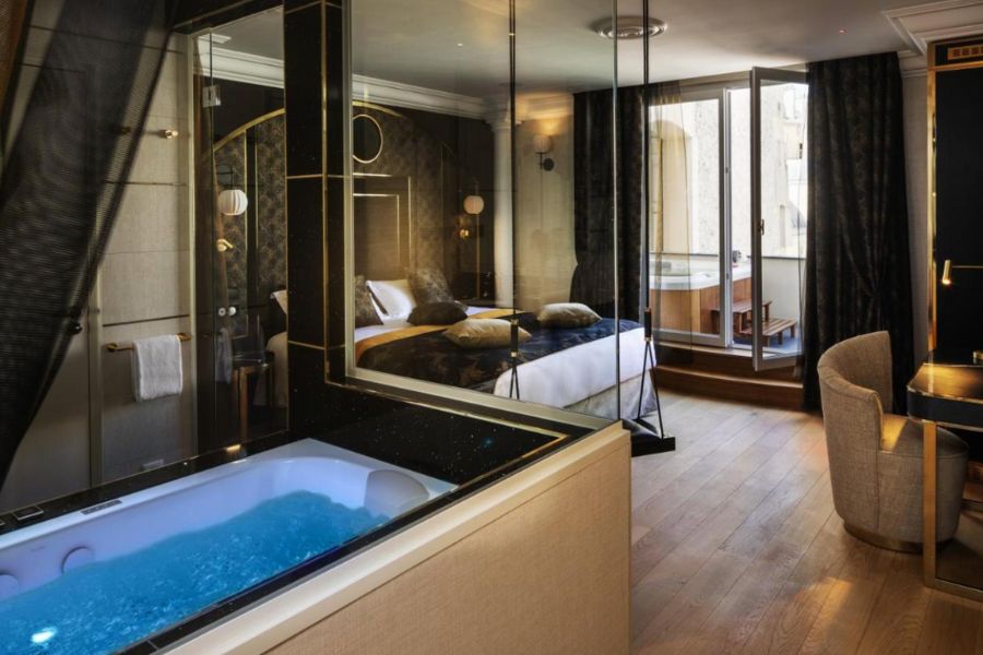 This is a picture of a spa hotel room. There is a very luxurious bed with a balcony, couch and spa alongside it. 
