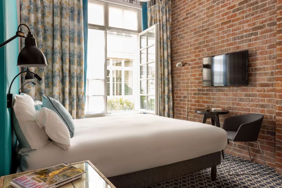 This is an image of a hotel room with a very minimal interior and exposed brick walls. 