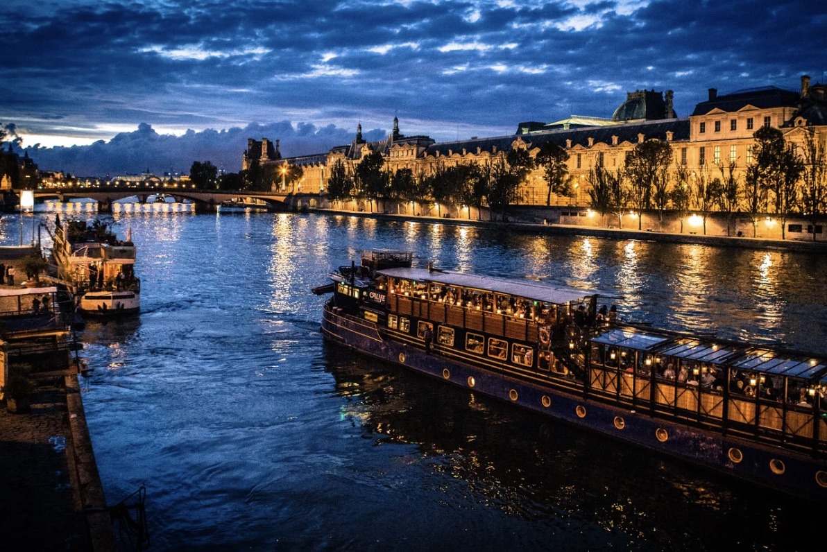 This is an image of a tour boat sailing through the Seine River. It is night, so there are lots of pretty lights.