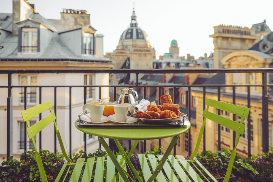 This is an image of a Parisian balcony with tables and chairs. There is also a view of lots of high buildings.