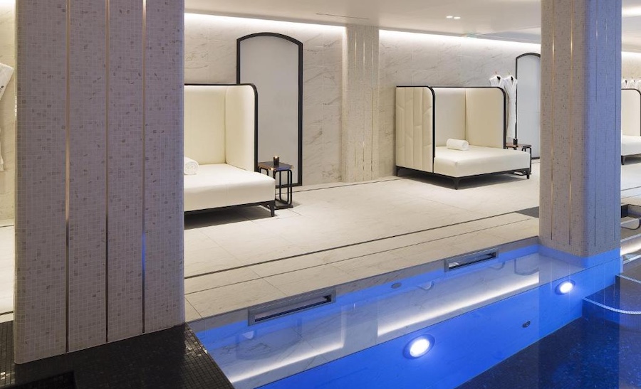 Beautiful and tall lounge chairs in white, on a marble floor next to a pool.