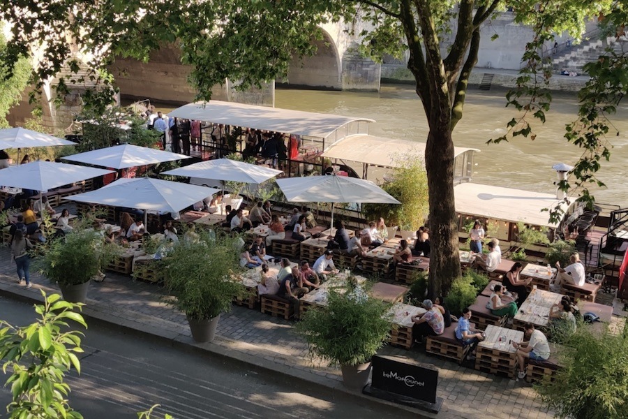 This is an image of a busy barge boat parked along the Seine. People are sitting on tables outside.