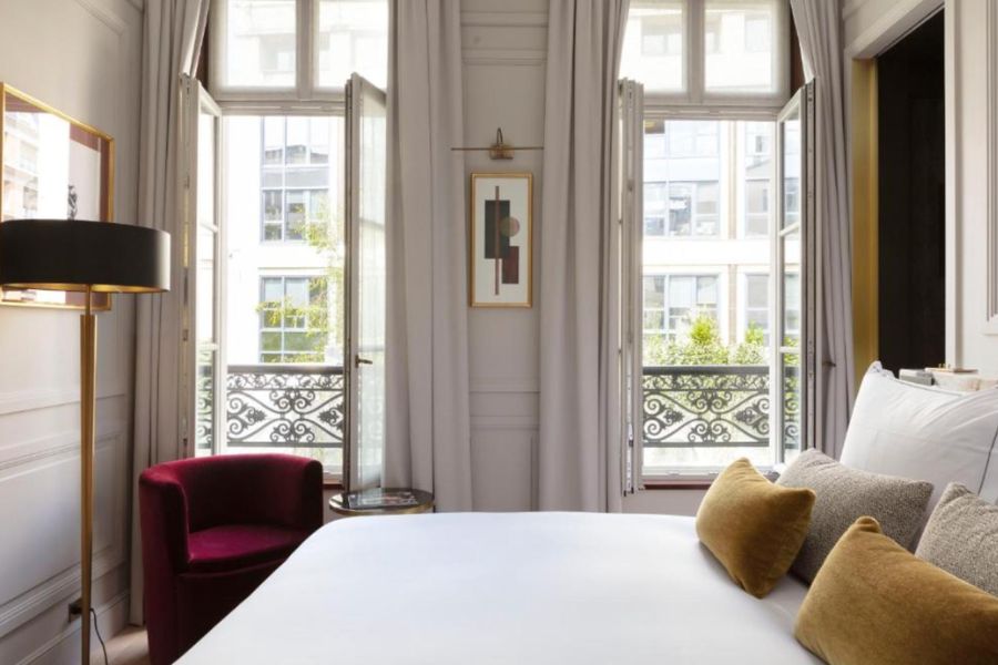 A classic Paris hotel room with tall French windows, wrought iron balconies, white walls and gold and burgundy accents