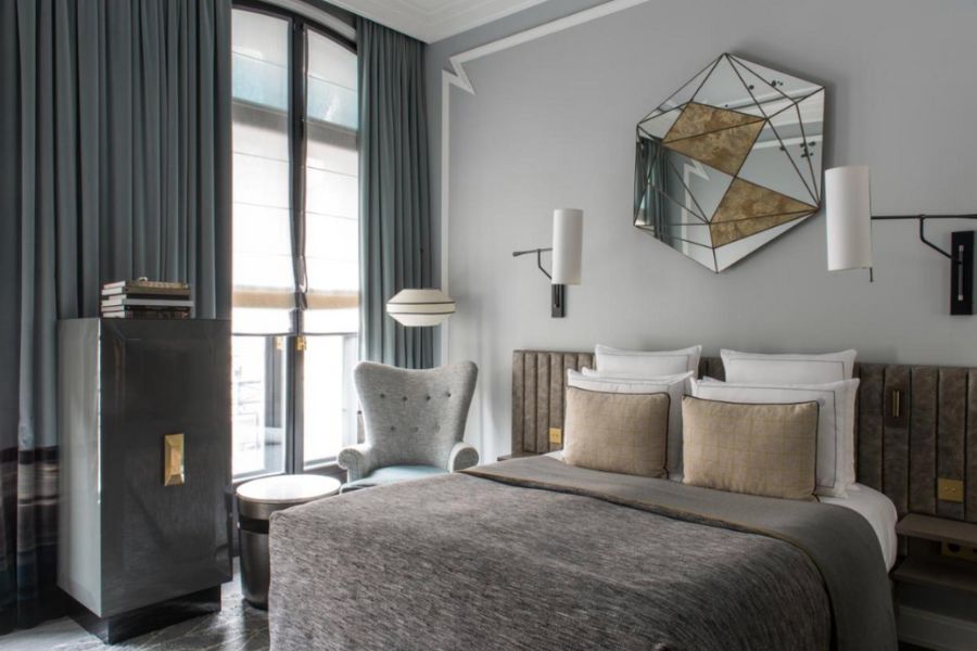 This is an image of a fancy hotel room in Paris. There is a mirror placed above the bed and big lamps to either side.