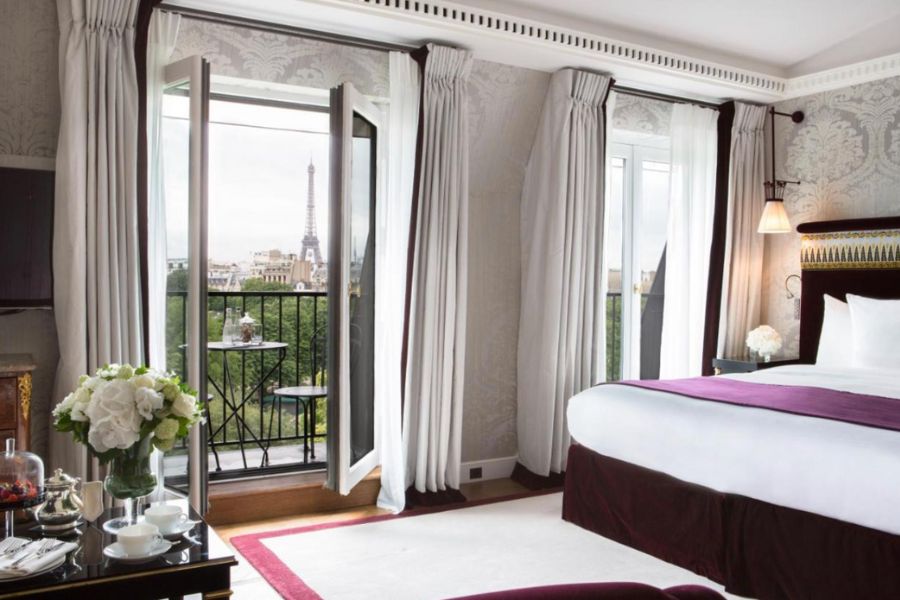 This is an image of a fancy hotel room in Paris with a balcony that looks out on to the Eiffel Tower.