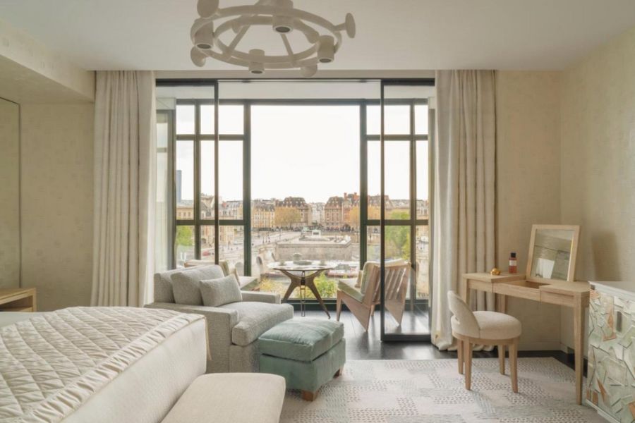 This is an image of a fancy hotel room in Paris with big French windows that looks out onto Parisian buildings.