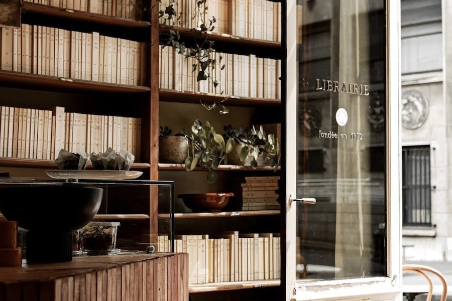 This is a picture of a little entryway to a cafe with books lining the shelves and plants hanging down.