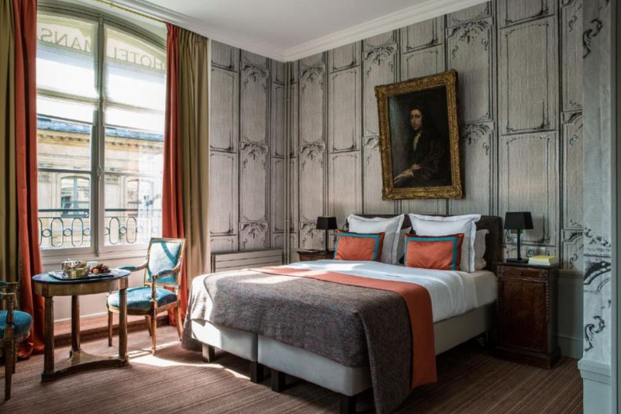 Refined hotel room with trompe-l'œil wood panelling wallpaper, a gilt-framed old master portrait, terracotta and teal accent cushions, and tall French windows