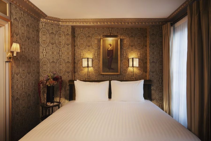 This is a small hotel room with a patterned feature wall. The double bed fills most of the room. It has a white duvet.