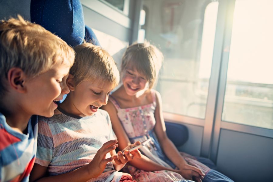 How to Pay for Kids on Public Transport in Paris: This is a picture of three kids sitting on a moving train all looking at the phone held in the middle boy's hand.