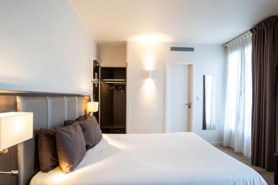 This is an image of a simple, minimalist hotel room with a double bed and a small wardrobe. 