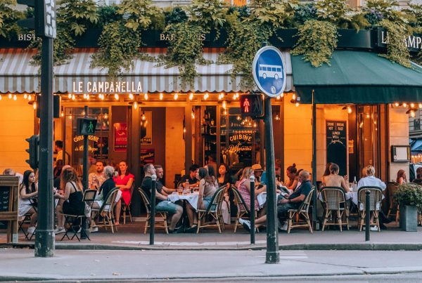 Places to eat with kids in Paris, with families dining at outdoor café tables beneath striped awnings and greenery.