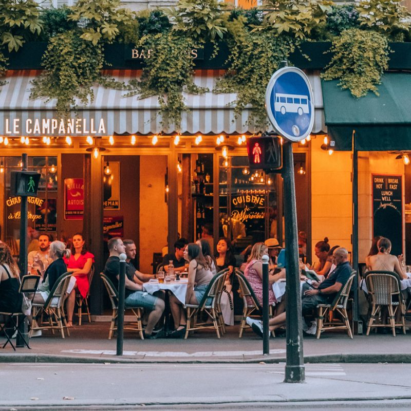 Places to eat with kids in Paris, with families dining at outdoor café tables beneath striped awnings and greenery.