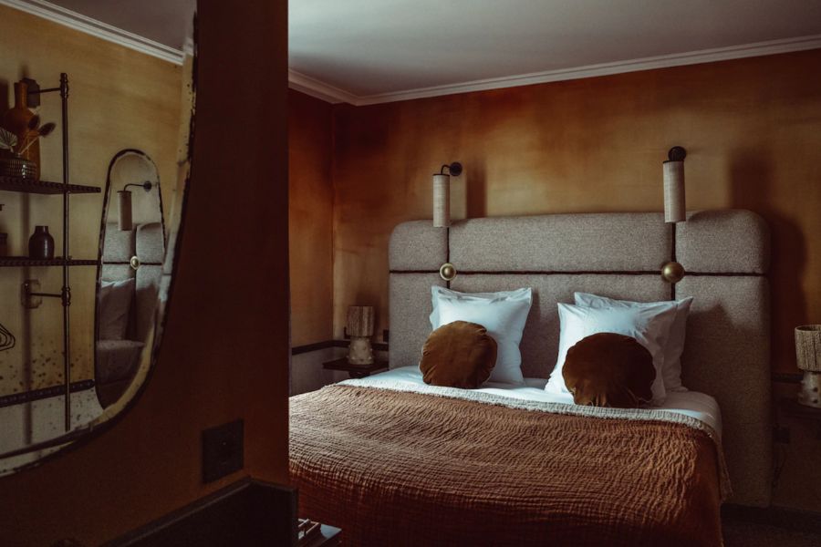 This is a picture of a very nice hotel room that has a burnt orange colour theme with plants and an eccentric mirror. 