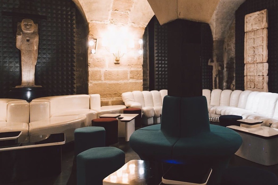 This is an image of a low-lit room with couches all around the space and cool stone walls with arches to create a more intimate, cosy space.