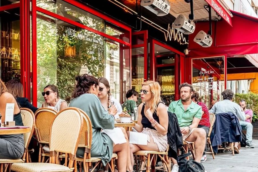 21:18Claude responded: People dining at outdoor café tables along a bustling Paris street in summerPeople dining at outdoor café tables along a bustling Paris street in summer
