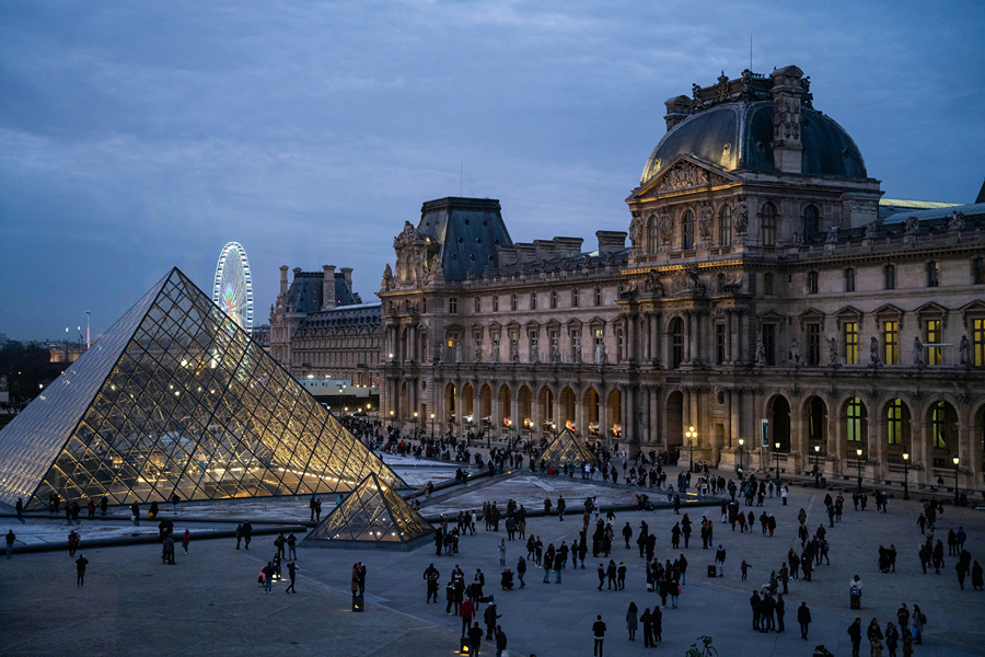 The Louvre Museum and illuminated glass pyramid at dusk, a beautiful Paris landmark to visit around Thanksgiving in Paris.