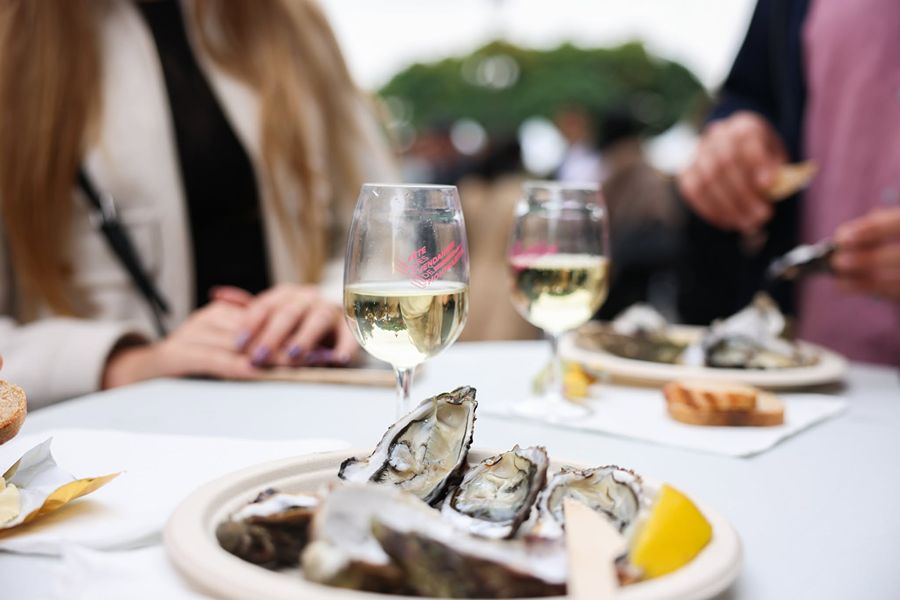 Glasses of white wine from the Fête des Vendanges de Montmartre and a plate of fresh oysters on a table at the festival