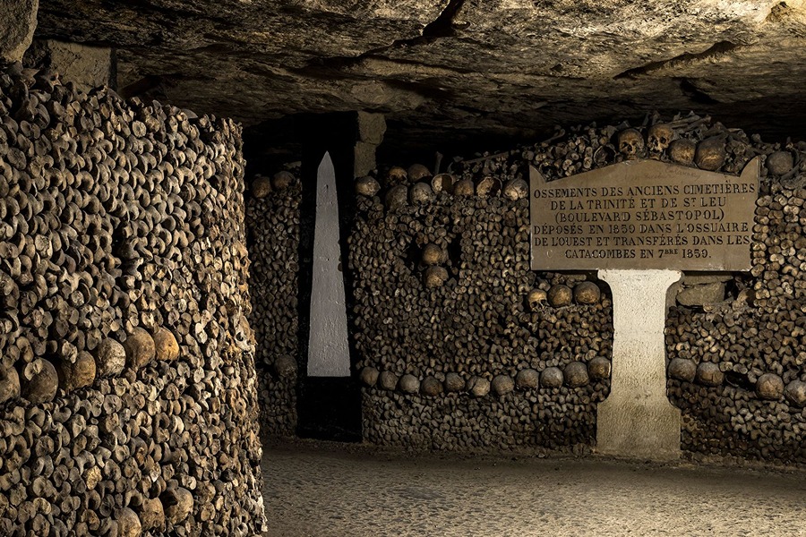 Rows of stacked bones and skulls lining a dimly lit tunnel in the Paris Catacombs