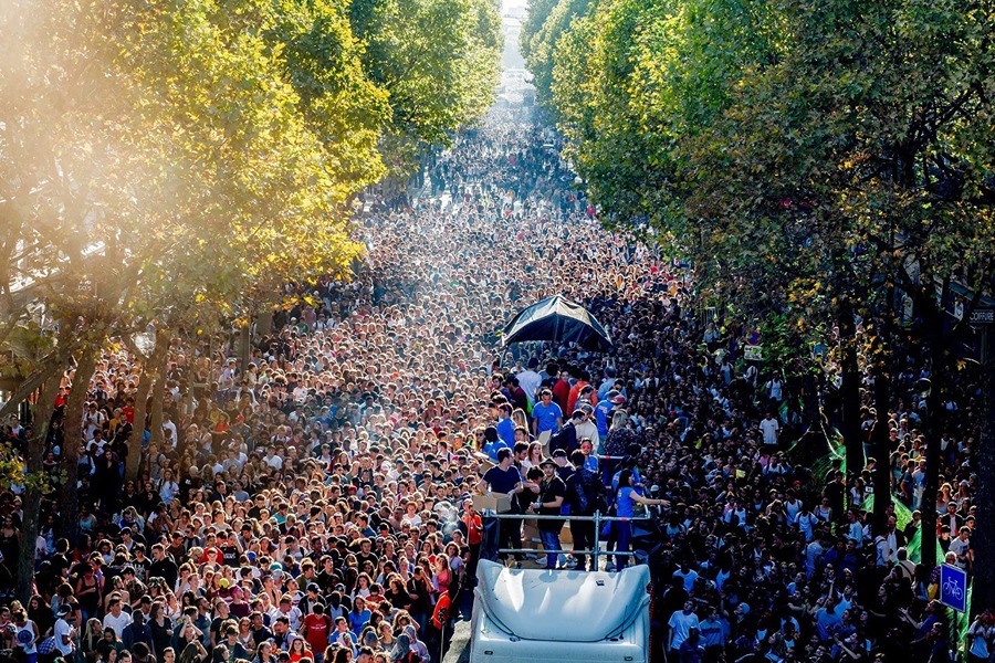 A huge crowd dancing along a tree-lined street at the Techno Parade, one of the best things to do in September in Paris.