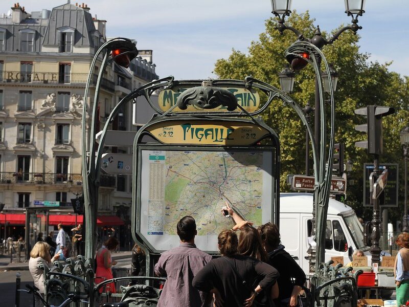 This is a picture of the entrance of Pigalle metro station in Paris. There are people on the outside looking at the map before going in.