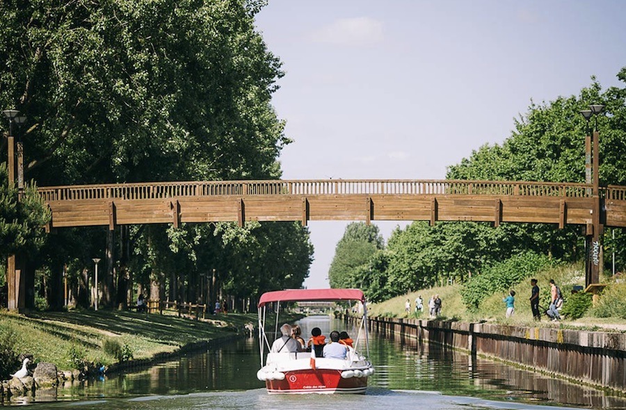 This is an image of a Parisian canal, where you can see a bridge in the distance as well as a small tour boat gliding through the water.