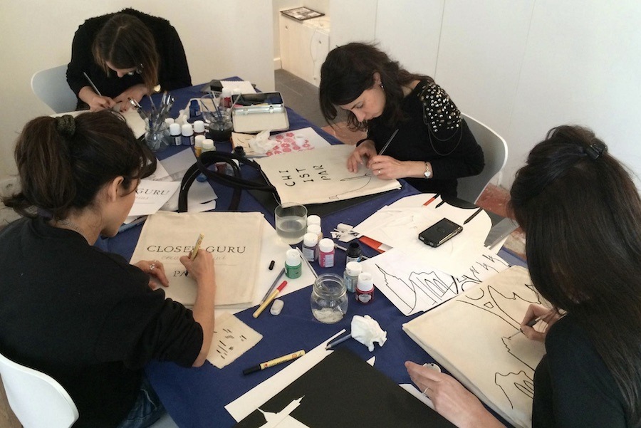 This is an image of a small group surrounded by paints and brushes decorating canvas tote bags. Tote bag decorating is a unique experience to try in Paris.