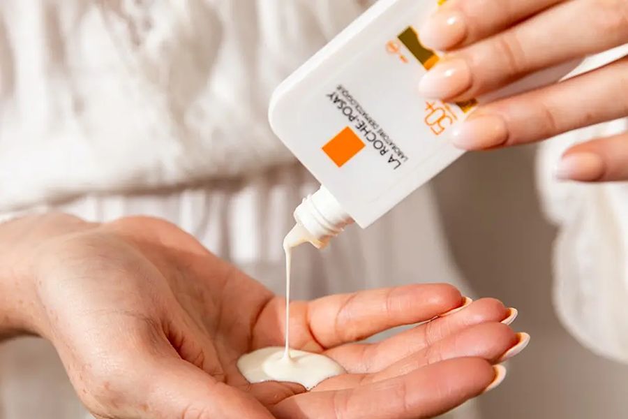 Close-up of hands squeezing white sunscreen lotion from a La Roche-Posay bottle into an open palm.