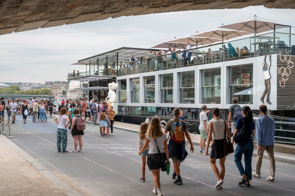 A lively river bar. Lots of people walk towards it.
