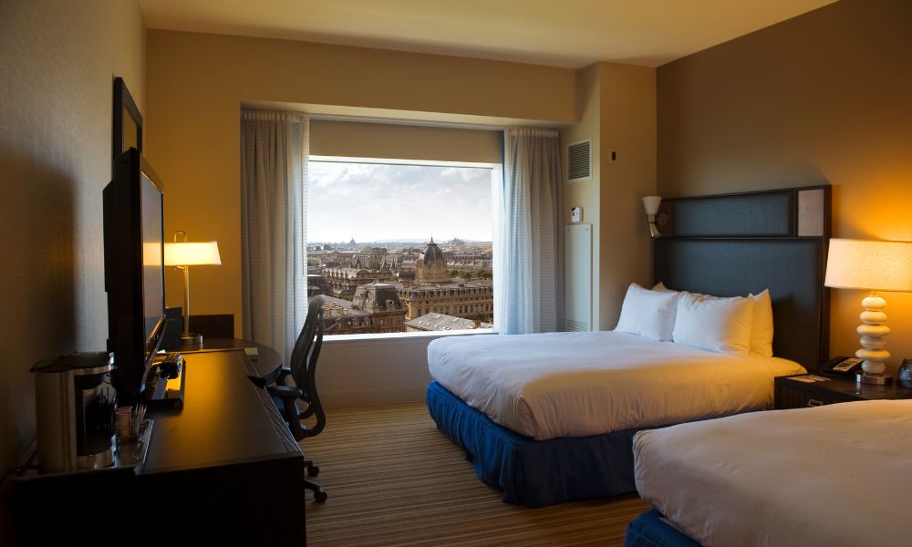 This is an image of a hotel room with two large beds and a view of Paris city out the window.