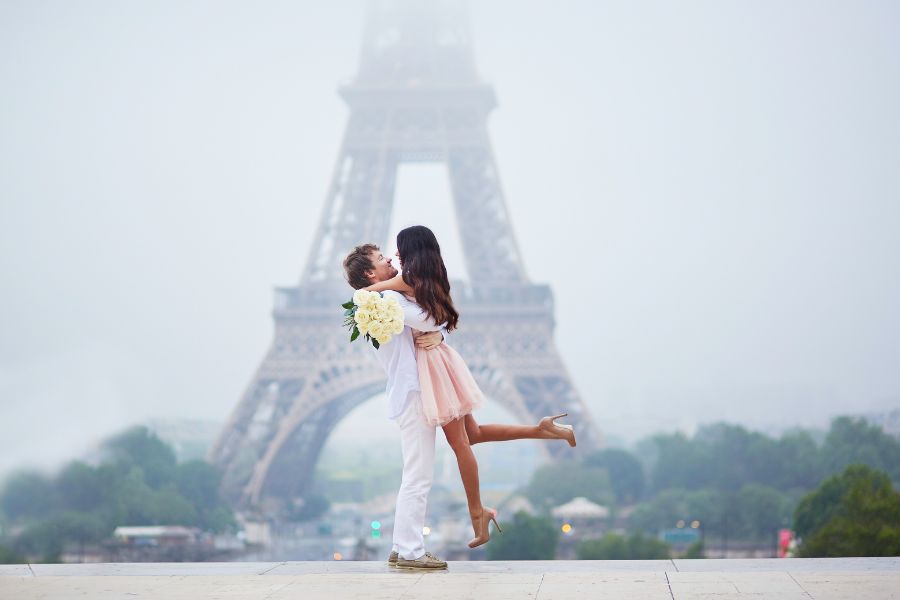 This is an image of a couple posing in front of the Eiffel Tower lovingly.