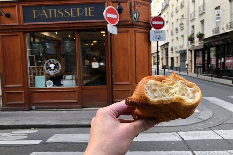 This is a picture of a person holding a half-eaten croissant in front of a shop.