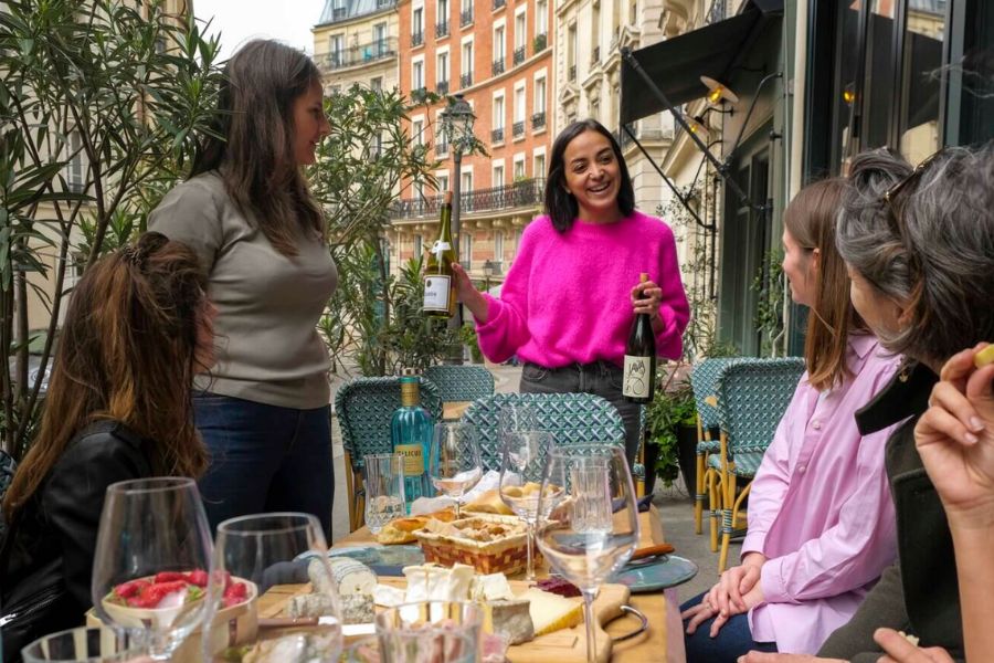 This is an image of a tour group sitting around a table enjoying fine french food with a lady pouring them wine.