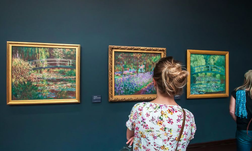 This is an image of a lady staring into a picture frame with some of Monet's work on it.