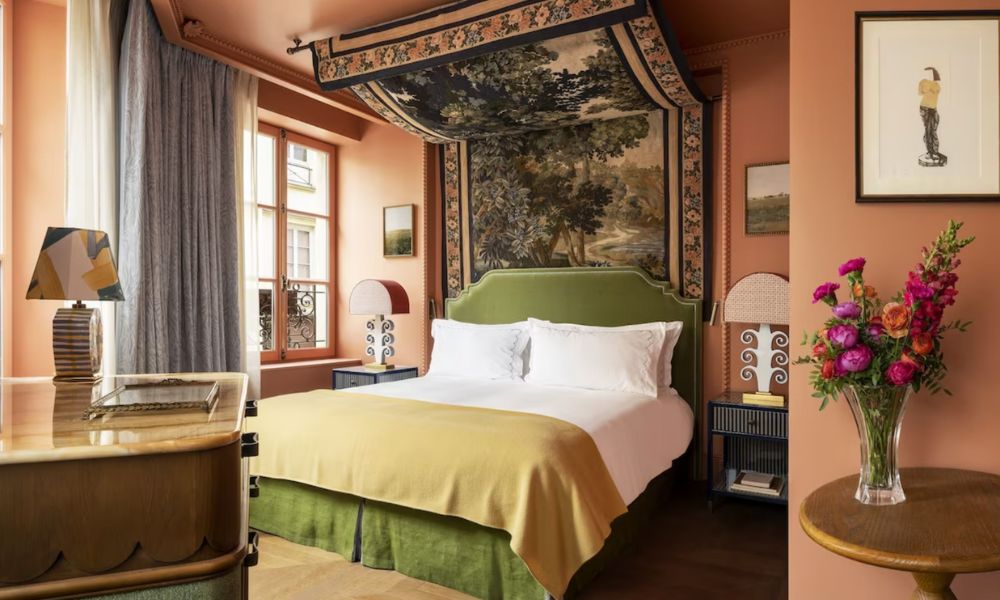 This is an image of a big hotel room with a double bed, a vase of flowers and a big feature carpet draping over the bed.