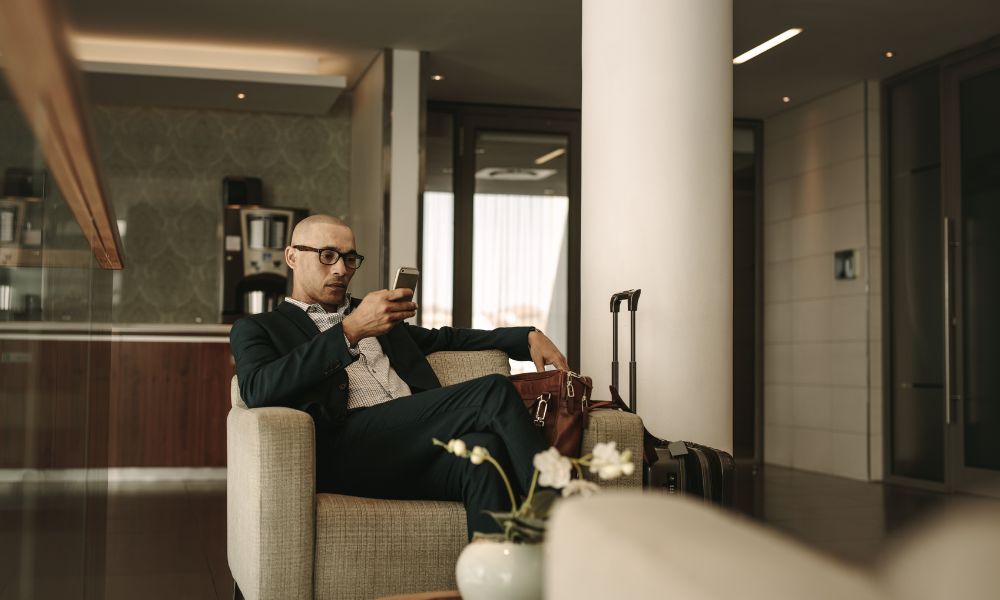 This is an image of a man in the business lounge on his phone with his suitcase beside him.