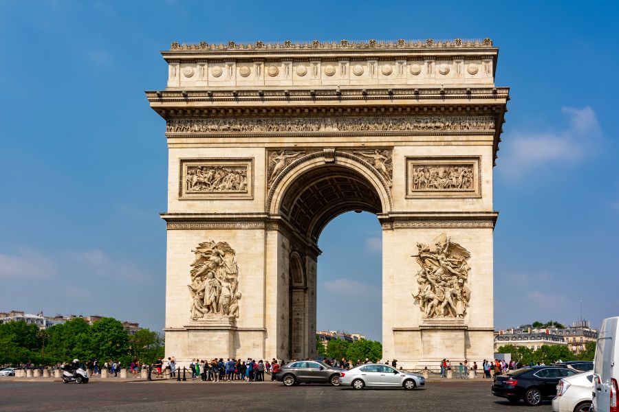 This is an image of the Arc De Triomphe and its surrounding roundabout on a sunny day with blue skies.