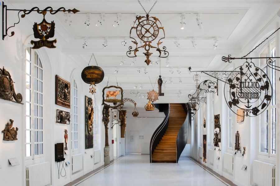 This is an image of a unique museum in Paris with cool trinkets lining the walls and a big staircase at the end.