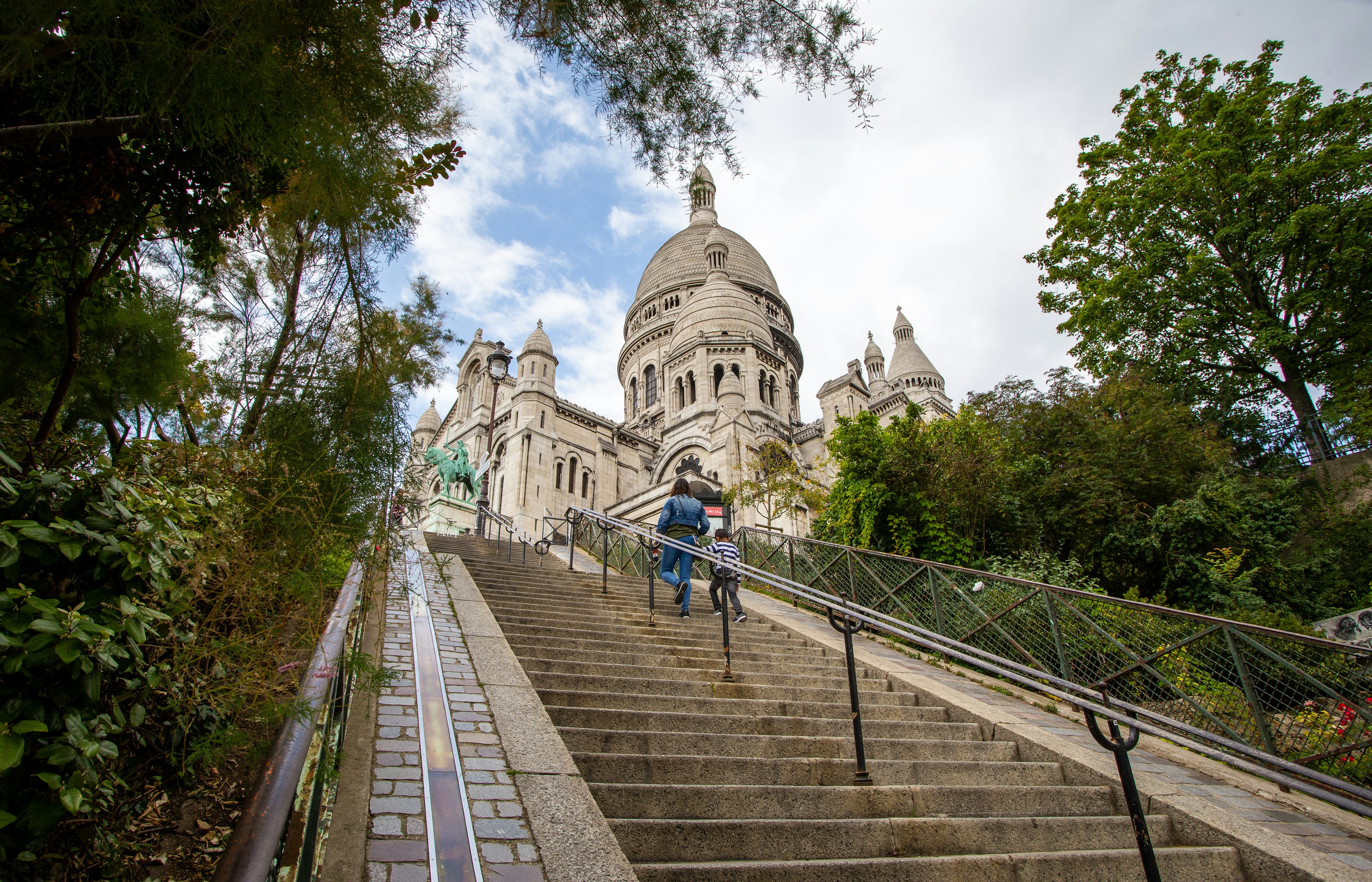 A steep set of stairs towards the sacre coeur. Flanked by lush green trees.