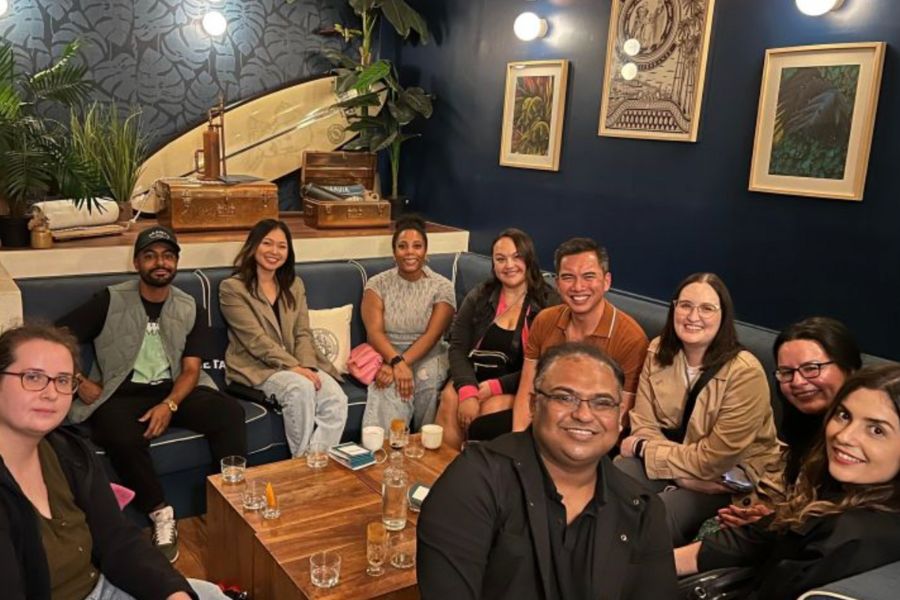 This is an image of a big group of solo travellers from all walks of life having a drink together at a bar and smiling for the photo.