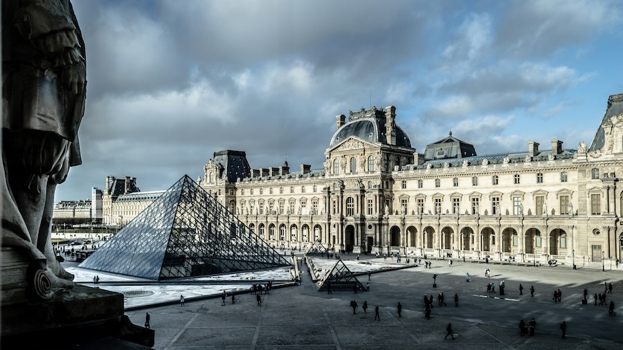 This is a picture of the Louvre. There are a few people milling around the area.