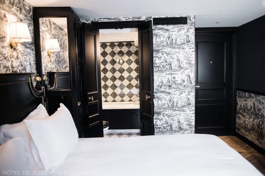 This is an image of a hotel room with marble, funky wallpaper and checkerboard bathroom features with a big double bed in the middle.